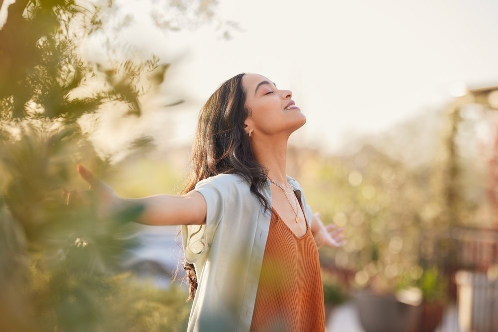 Happy young woman with arms outstretched breathing in fresh air during sunrise.
