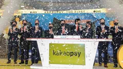 People clapping behind a podium with the Kakao Pay logo on it and confetti in the air at the payments provider’s debut on the Korea Exchange in 2021