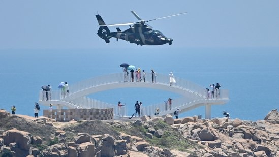Tourists look on as a Chinese military helicopter flies past Pingtan island, one of mainland China's closest point from Taiwan, in Fujian province on August 4, 2022, ahead of massive military drills off Taiwan following US House Speaker Nancy Pelosi's visit to the self-ruled island. China is due on August 4 to kick off its largest-ever military exercises encircling Taiwan, in a show of force straddling vital international shipping lanes following a visit to the self-ruled island by US House Speaker Nancy Pelosi.  (Photo by Hector RETAMAL / AFP)