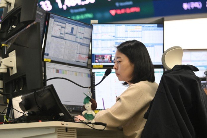 A female currency dealer is focused on multiple computer monitors displaying financial data
