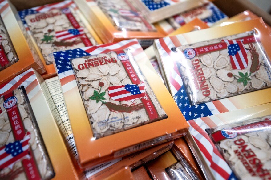 Packages of dried American ginseng with English and Chinese text and U.S. flag motifs are stacked together in a box.