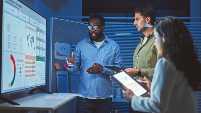 Discussion between three people standing in front of a monitor.