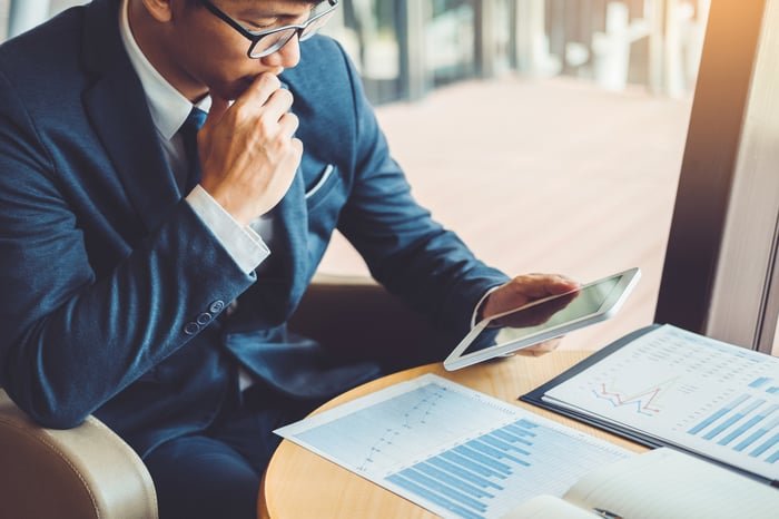 A person examining stock price charts on paper and a digital tablet.