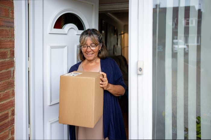 A happy consumer picks up a cardboard 
box package from their doorstep.