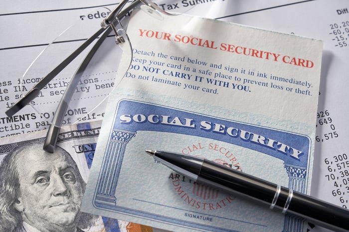 A pen laying on top of a Social Security card alongside a pair of glasses and $100 bill.
