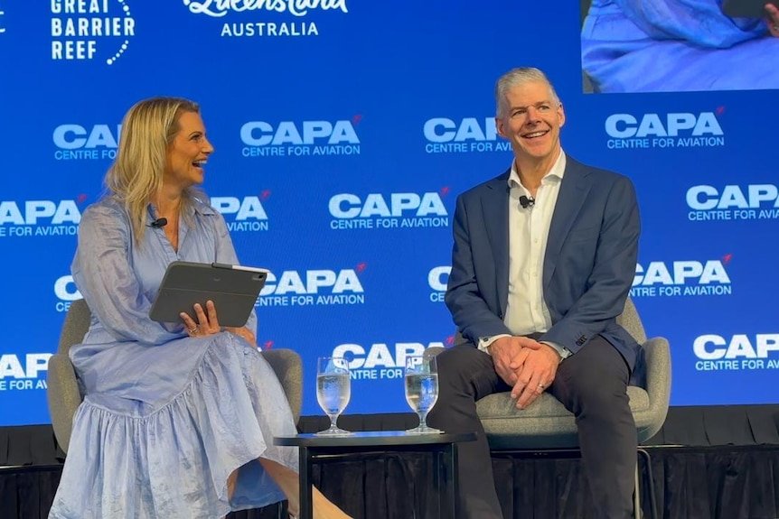 A man and woman sitting on a stage at a conference with CAPA signs in background.