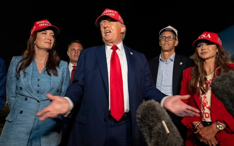 Donald Trump speaks with reporters in Iowa alongside Kristi Noem, right