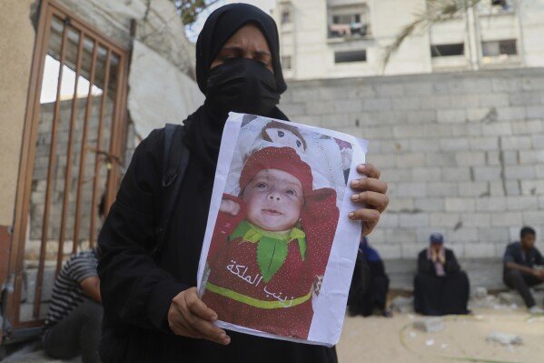 Esraa Abu Halib shows to journalists a photo of her 5-month-old baby, Zainab, who died from malnutrition-related causes, according to the family and the hospital, as she stands outside the Nasser Hospital, in Khan Younis, Gaza Strip, Saturday, July 26, 2025. (AP Photo/Mariam Dagga)