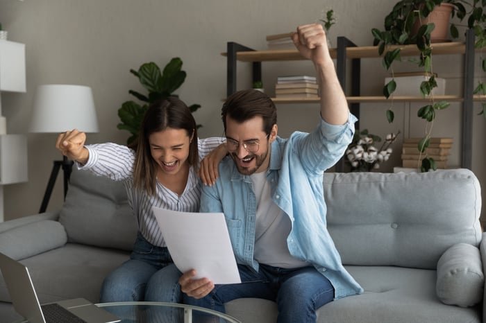 Two people looking at paper, smiling, and raising fists in air in celebration.