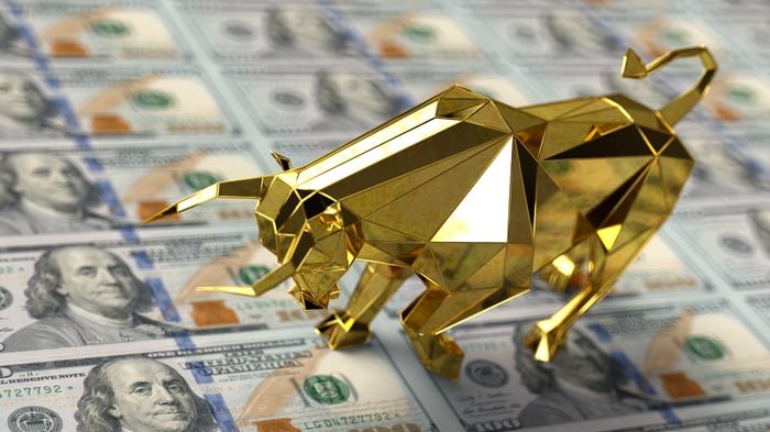 A gold bull figurine sitting on stacks of hundred dollar bills.