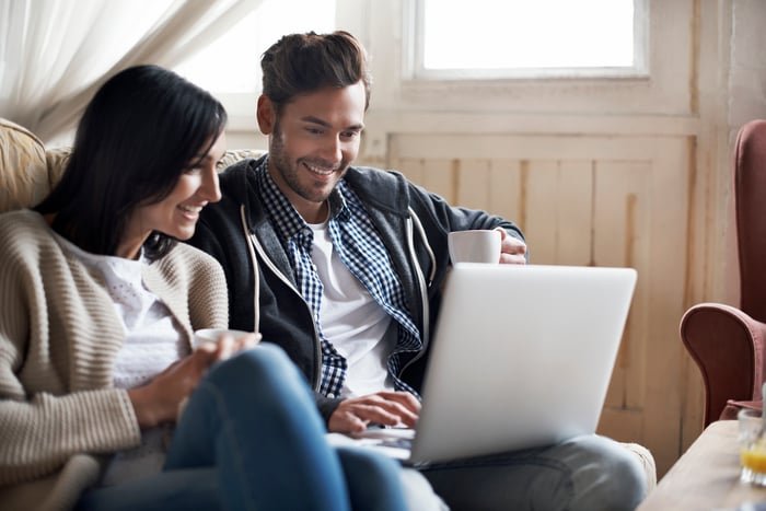 Two investors at home look at something on a laptop.