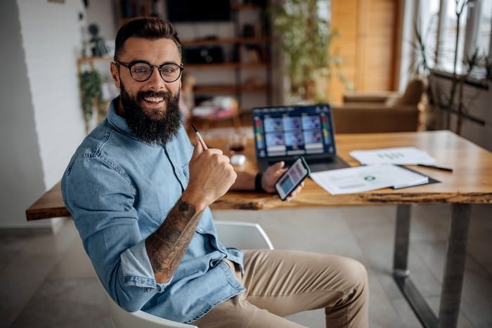 Happy person sitting with phone and laptop.