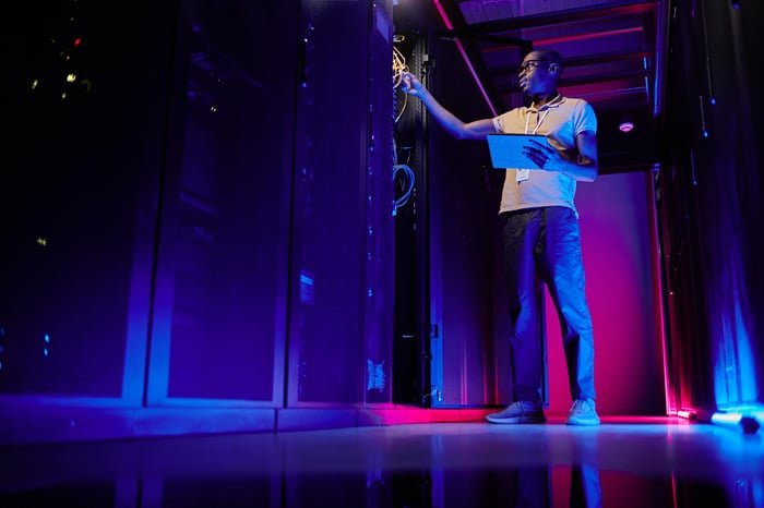 A system administrator setting up a server network in a data center lit by neon lights.