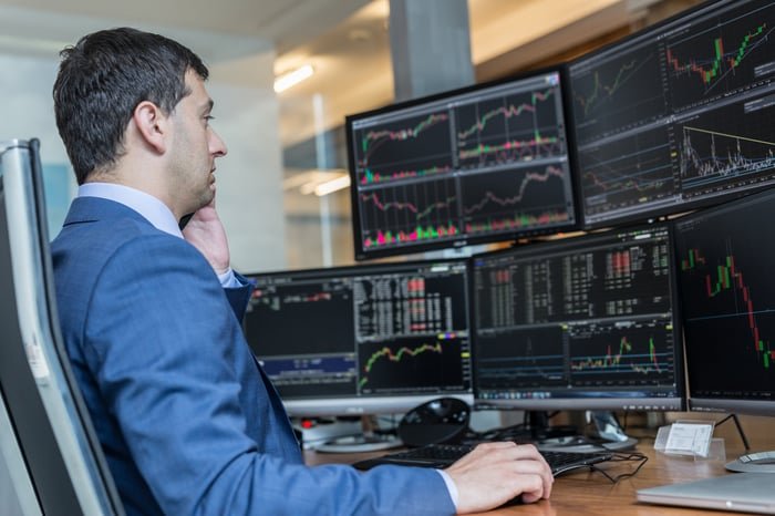 Person in front of multiple computer screens with stock charts on them,