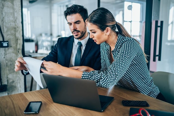 Two investors look at something on a clipboard in an office.