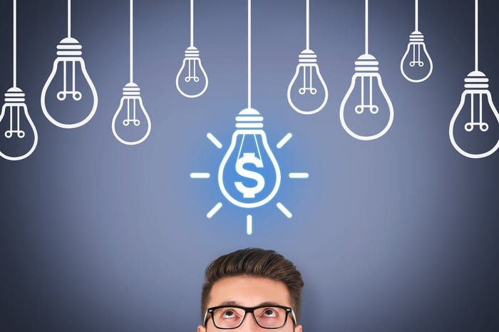 A person looking up at drawings of light bulbs and one bulb with a dollar sign.