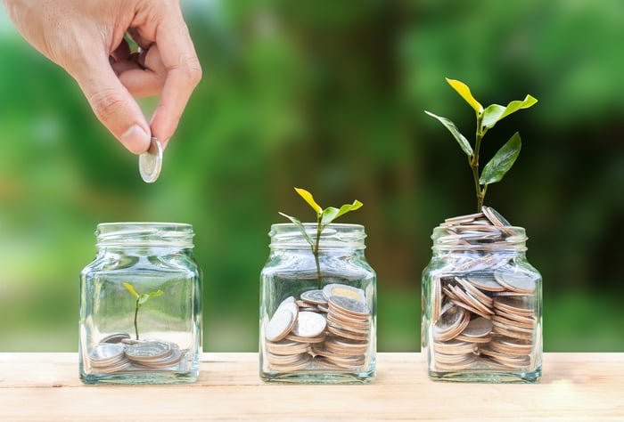 Hand putting coins into glass jars that are sprouting plants.