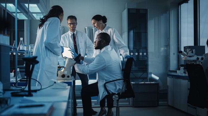 Four people wearing white lab coats in a lab.