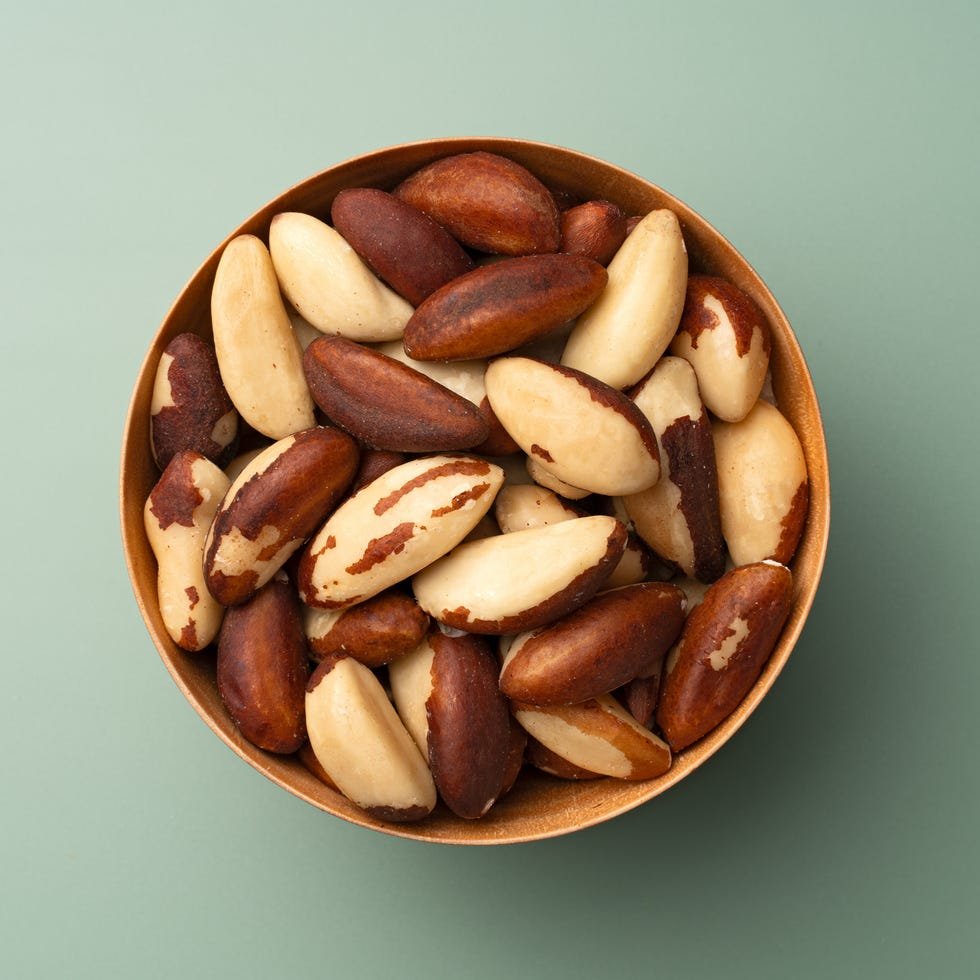brazil nuts in wooden bowl on green background