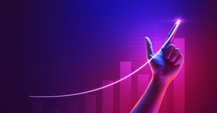 A person's hand pointing at a chart line going up.