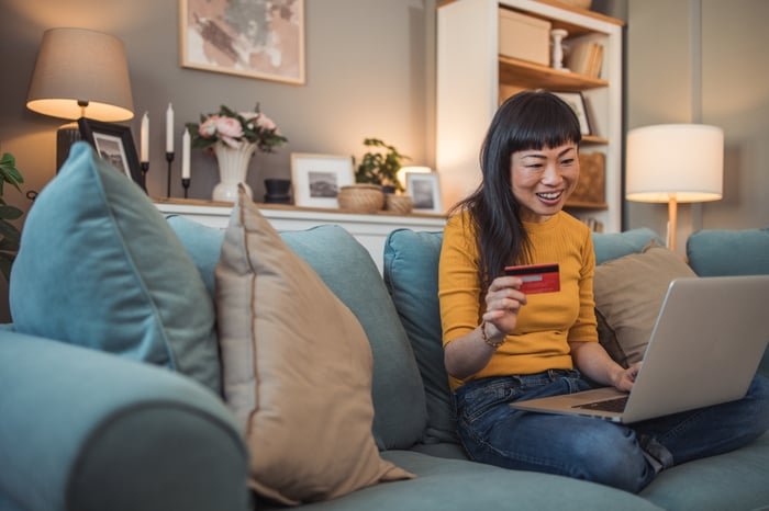 Person holding payment card while using a laptop PC.