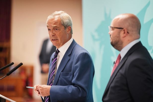Two men, one with grey hair and one who is bald with glasses, wearing suits