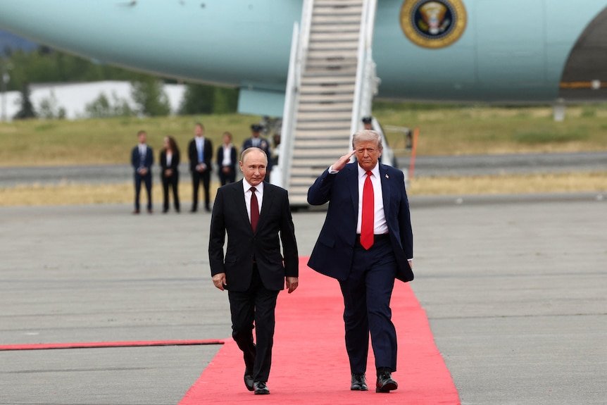 Donald Trump and Vladimir Putin walk along a red carpet on a tarmac.
