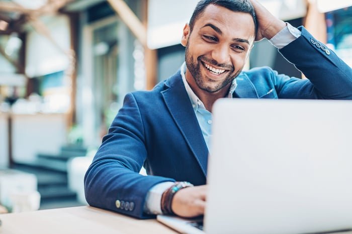 An investor smiles at something on a laptop screen.
