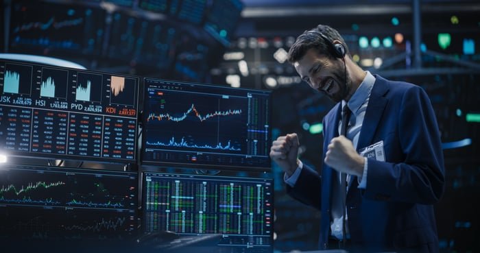 Trader celebrating in front of multiple monitors displaying market charts and financial data.