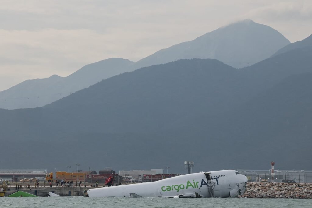 The broken fuselage of a cargo jet lies half submerged in water.