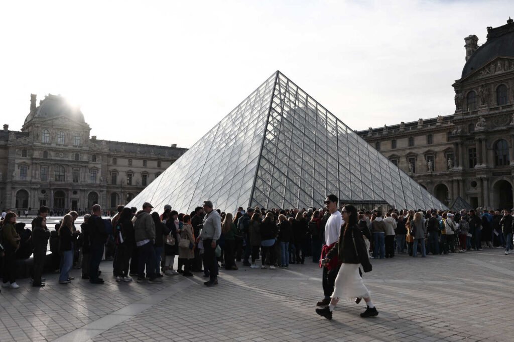 Lines of people outside the glass pyramid at the Louvre Museum in Paris.
