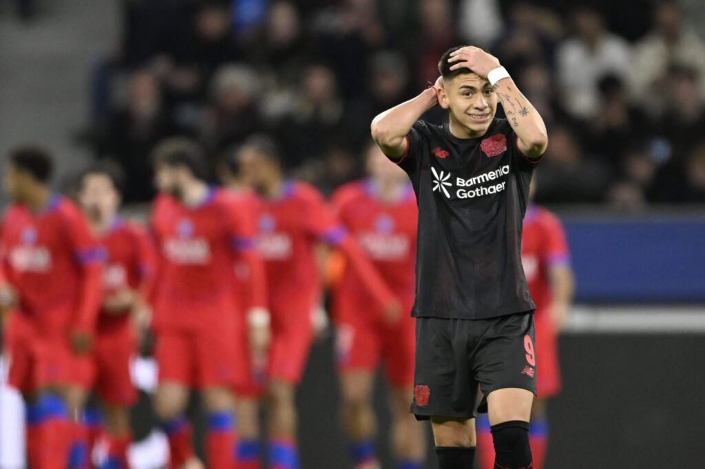 Bayer Leverkusen's Claudio Echeverri grimaces with his head on his hands as Paris Saint-Germain's players celebrate a goal in the background