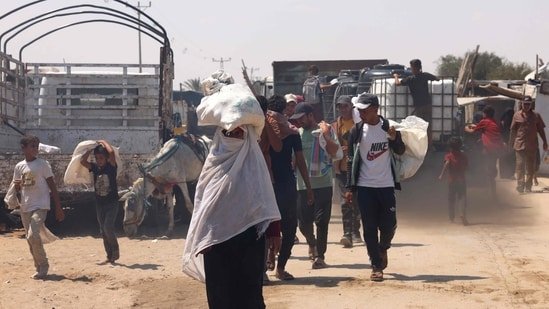 A Palestinian woman carries humanitarian aid, she gathered after an aid drop, as she walk in the Mawasi area of Rafah in the southern Gaza Strip on August 18, 2025. (AFP)
