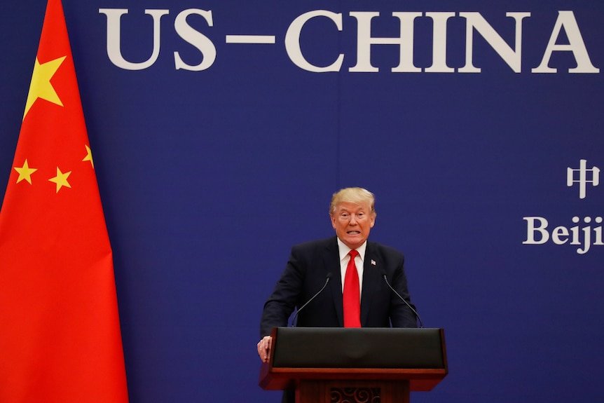 Man stands next to Chinese flag at a podium