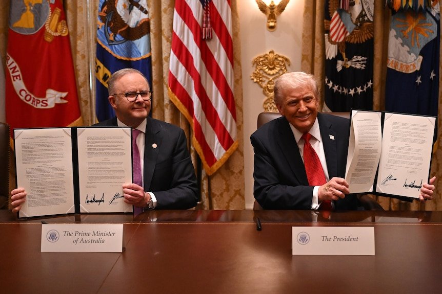 Anthony Albanese and Donald Trump hold up signed documents in front of flags