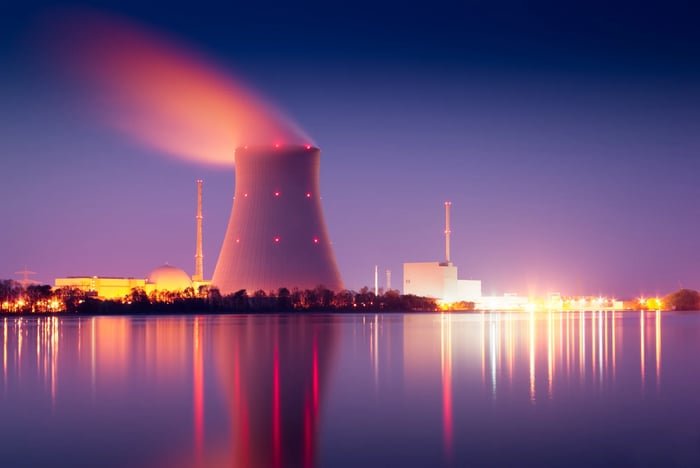 Nuclear power plant at night, illuminated by bright lights, and reflected in a body of water below.