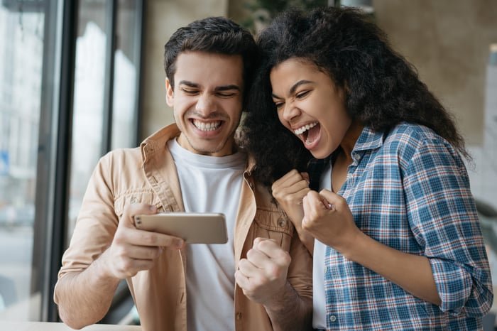 Two people react to an event on one's smartphone.