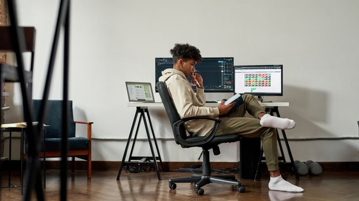 investor studies book with stock charts on computer screens.