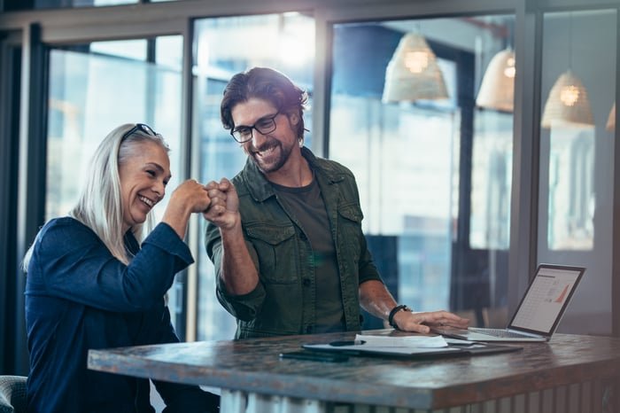 Two investors bump fists and smile in an office.