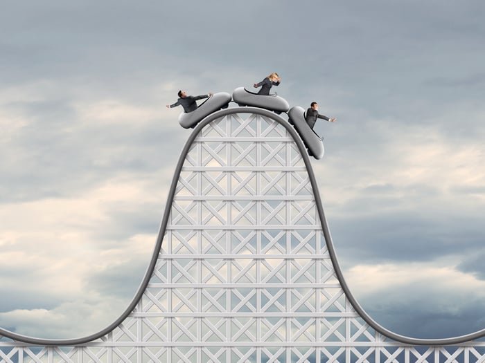 Three people in cars at the top of a rollercoaster.