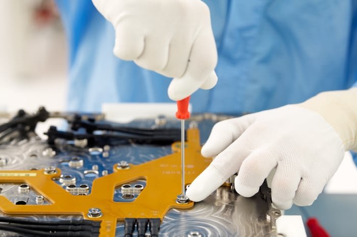 Person wearing gloves working on a circuit board.